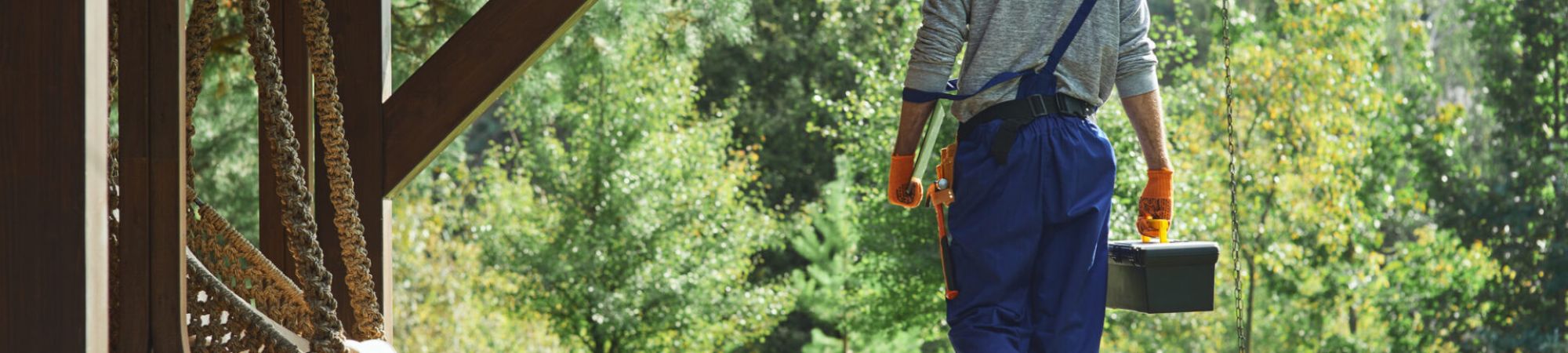 Full length shot of young workman in uniform walking with toolbox after doing repair work in the cottage house on a sunny summer day. Profession concept. Rear view