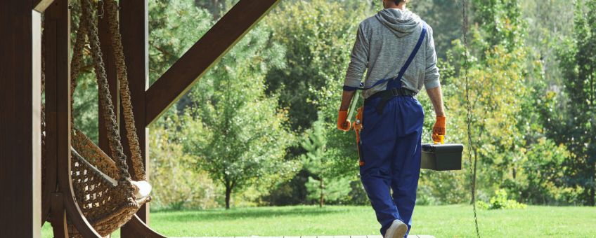 Full length shot of young workman in uniform walking with toolbox after doing repair work in the cottage house on a sunny summer day. Profession concept. Rear view